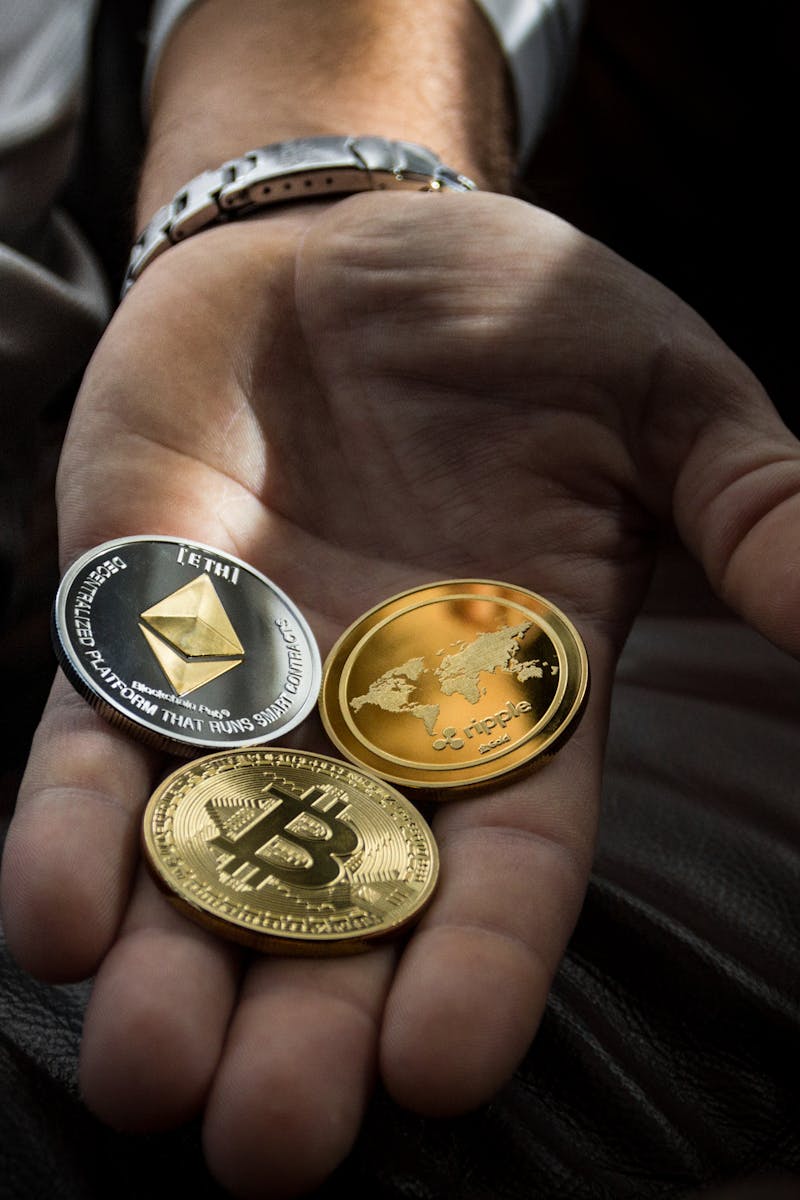 Hand holding Bitcoin, Ethereum, and Ripple coins representing digital currency.