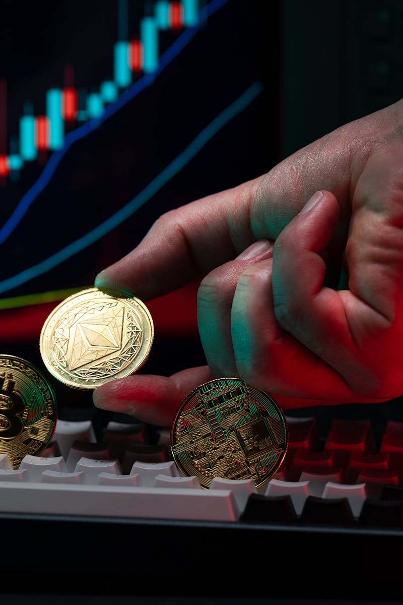 Close-up of a hand holding cryptocurrency coins on keyboard, with a graph display in the background.